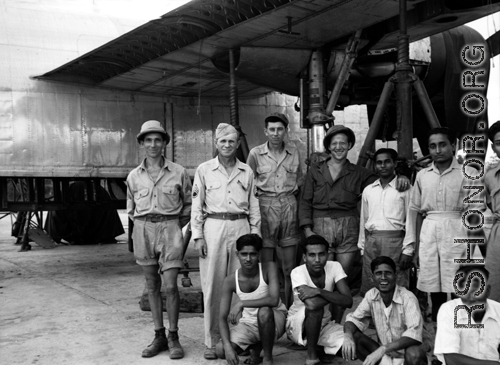 American and Indian service crew members pose for the camera in front of a B-24 up on jack and undergoing maintenance. 61st Air Service Group.