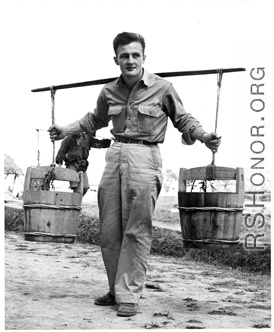 GI poses with buckets on a shoulder pole in China, during WWII.