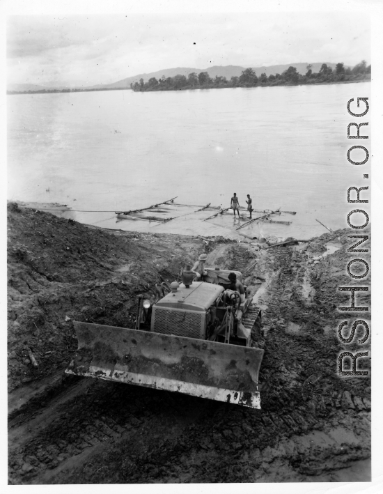 Cat pulling logs raft up bank from river.  797th Engineer Forestry Company in Burma.  During WWII.