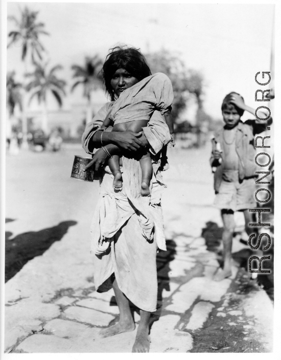 Begging woman holds child on road in town in Burma or India.  Near the 797th Engineer Forestry Company.  During WWII.