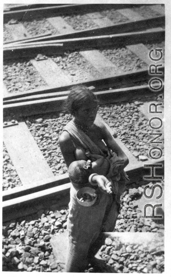 Breastfeeding beggar and infant along railroad tracks, likely in India, during WWII.