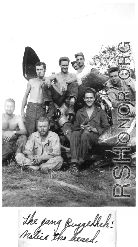 Boys of the 2005th Ordnance Maintenance Company, 28th Air Depot Group, sitting of the engine of a wrecked airplane, in Burma. During WWII. One is holding a puppy--their "mascot" named "Evan." John Schuhart sitting cross-legged with cigarette. 