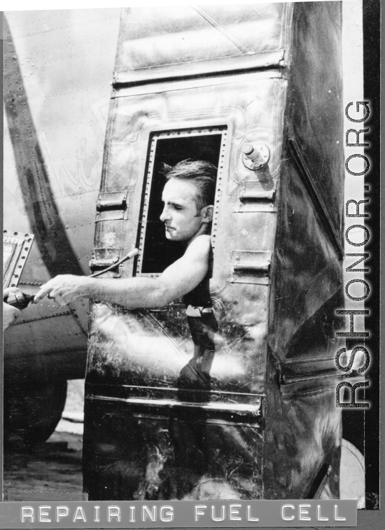Engineer repairing fuel cell--from inside--during WWII. A B-24 or F-7 is in the background.