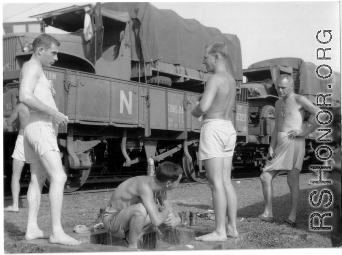 US soldiers bathing at a faucet during war, alongside a railway.