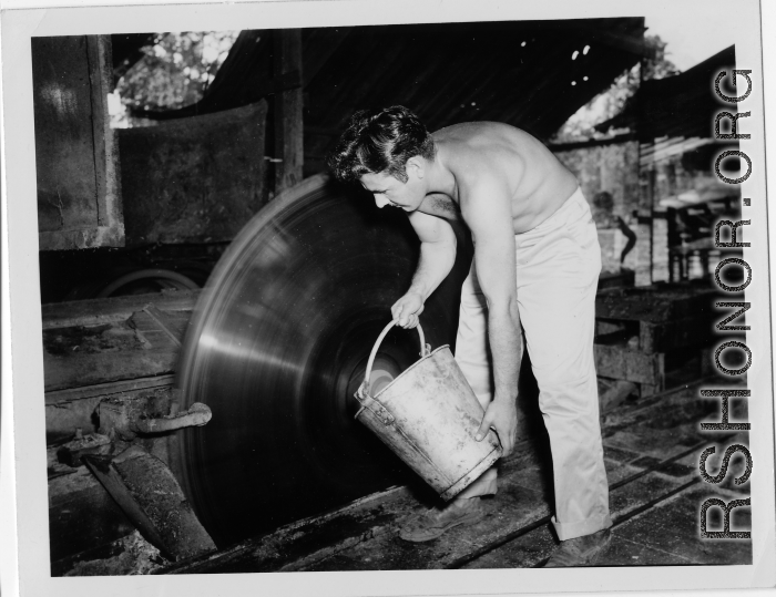 GI of the 797th Engineer Forestry Company in Burma, dousing spinning deadly saw blade with water, for cooling or cleaning.  During WWII.