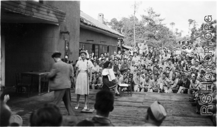 Celebrities (including Ann Sheridan, Ben Blue, and and Ruth Dennis playing an instrument in this shot) perform on an outdoor stage set up at the "Last Resort" at Yangkai, Yunnan province, during WWII. Notice both Americans and Chinese in the audience for this USO event.