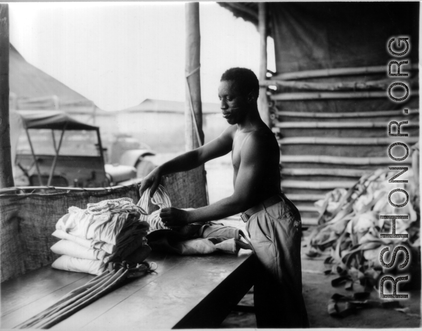 An African-American serviceman carefully packs a parachute for use by aircrews in emergency bailouts, in some location in the CBI where the weather was hot.