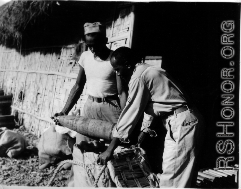 Two African-American soldiers load artillery shells into canvas-wrapped bamboo baskets for transport in the CBI during WWII.