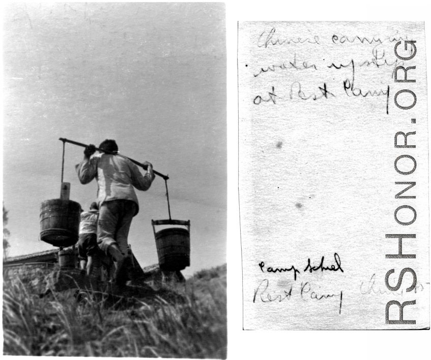 A Chinese laborer carries large buckets of water on a pole up the hill towards the accommodations at Camp Schiel during WWII.
