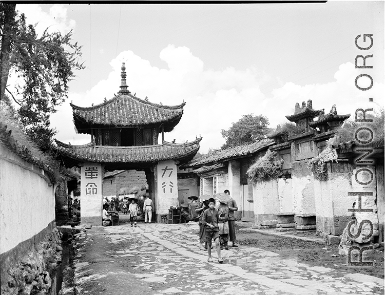 A whitewashed village street in Luliang, Yunnan, China, with a small gate tower towards the left, and ceremonial arch on the right. Local people in China.
