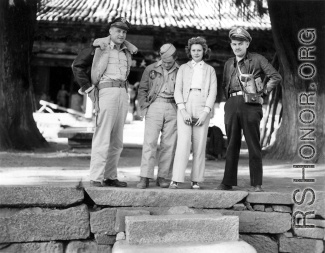 Americans in the China--armed with pistols and cameras--pose under the shade of large ancient trees outside a temple building. During WWII.