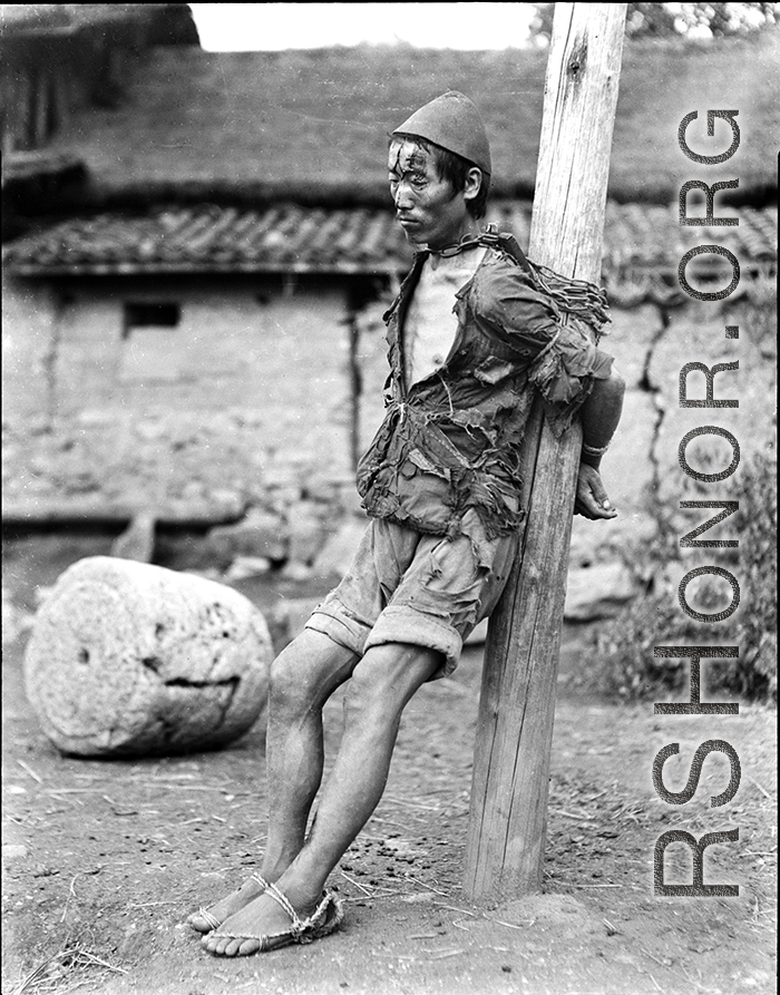 An impoverished possible criminal or suspect tied to a post in WWII China, as a form of punishment.