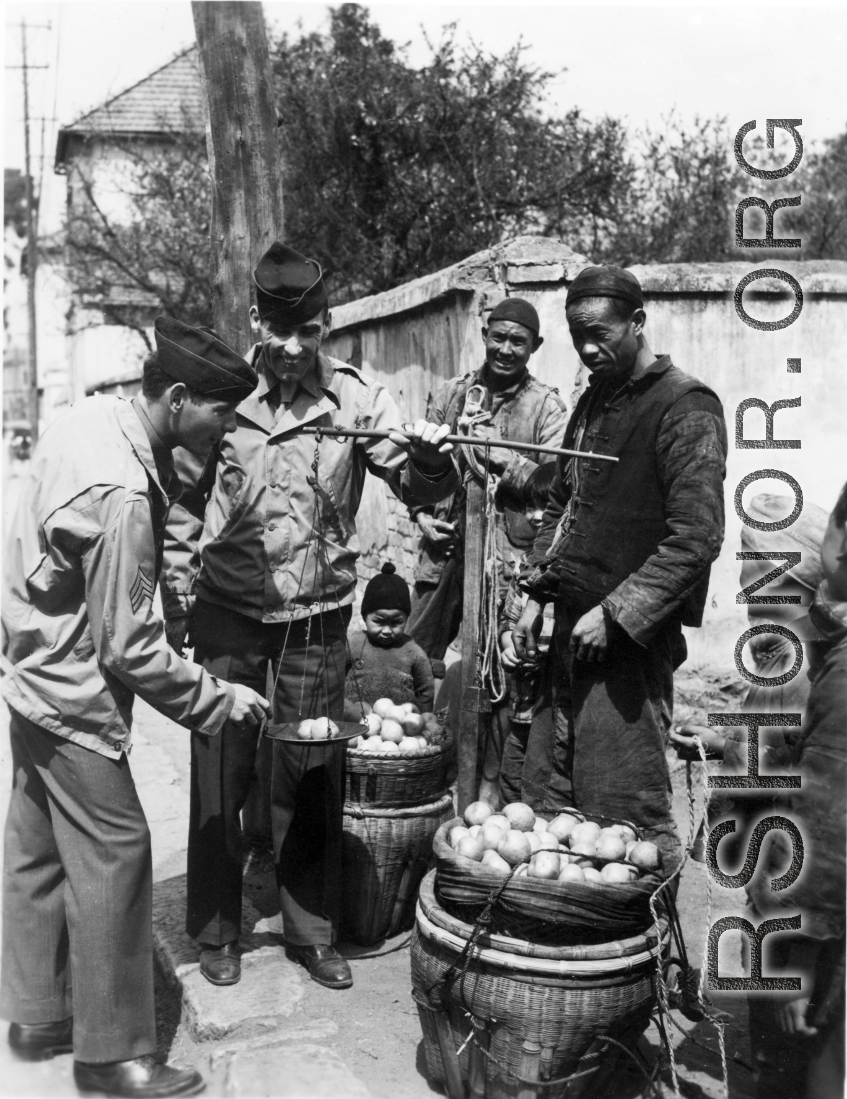 GIs buy citrus from farmers in China during WWII. These might be the amazing regional penggan (椪柑), somewhat similar to a mandarin orange.  Americans and Chinese interact at the market, China.  From the collection of Wozniak, combat photographer for the 491st Bomb Squadron, in the CBI.