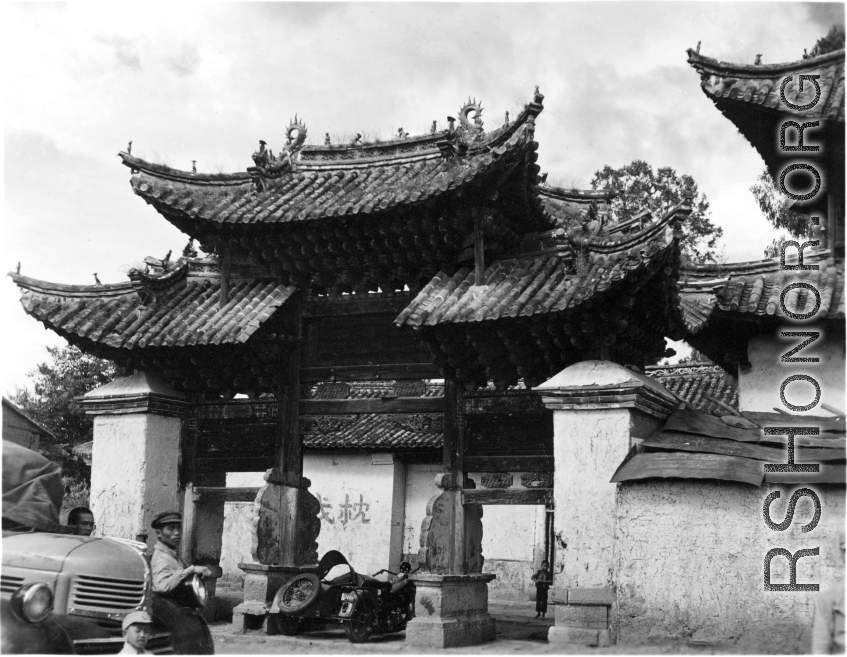 Men waiting near a memorial archway. Local people and architecture in Yunnan province, China, during WWII.