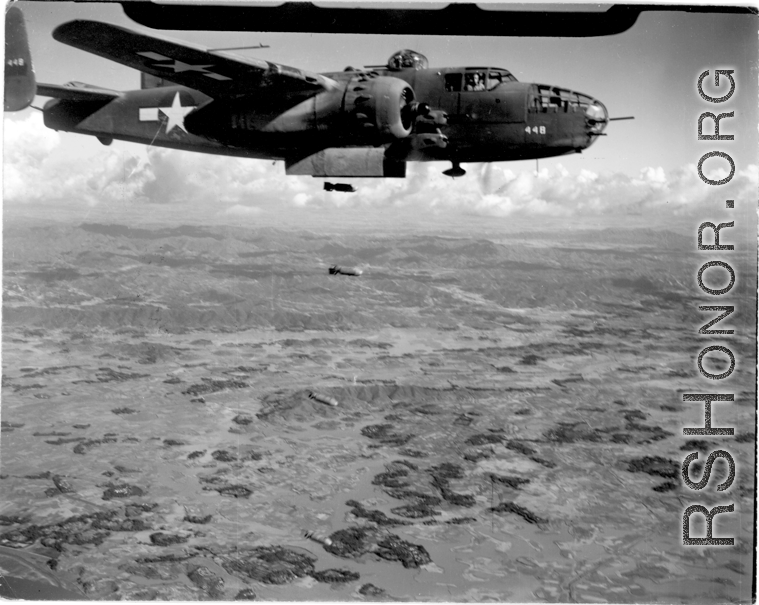 A B-25 Mitchell bomber, #448, in flight and dropping bombs in the CBI, in the area of southern China, Indochina, or Burma.