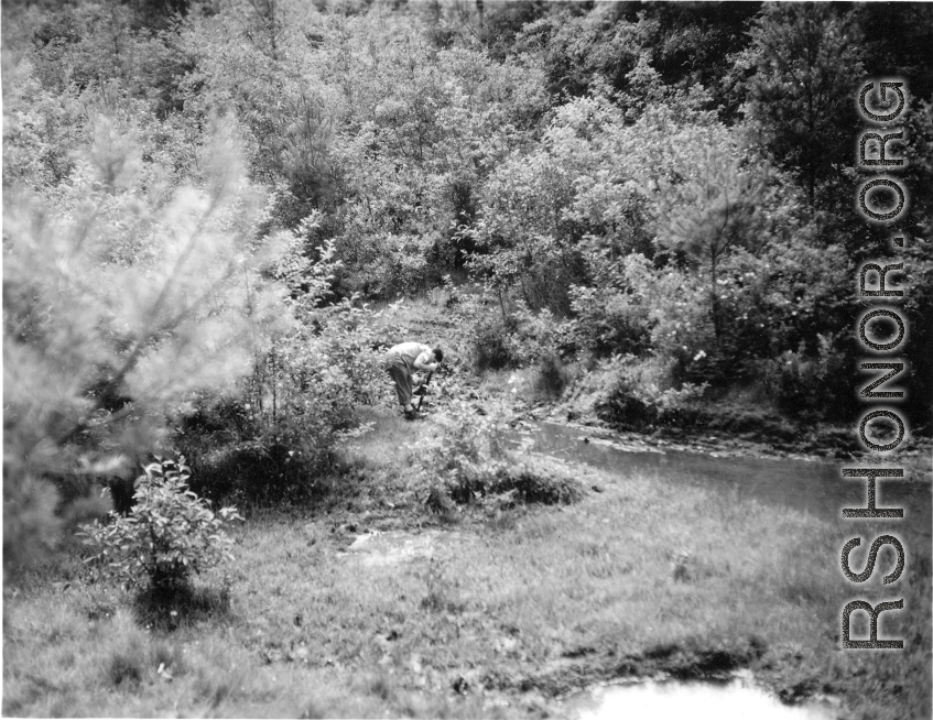 An American soldier fusses over something near a stream in Yunnan province, China, during WWII.