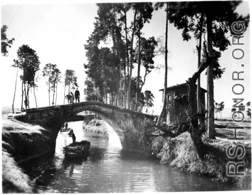 A boat on a canal near a small bridge in rural Yunnan province, China, with American GIs looking on from bridge above. During WWII.