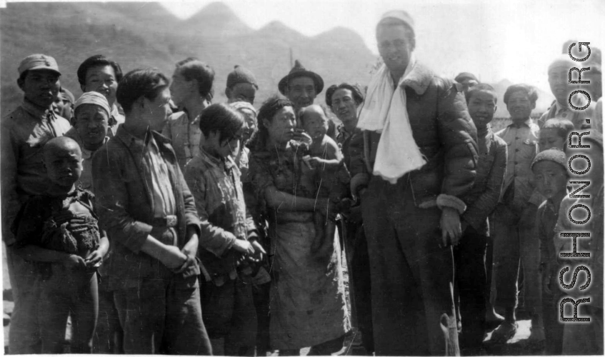 An American flyer--piece of silk parachute slung around his neck--is surrounded by appreciative crowd of Chinese people in Guangxi, China. During WWII.