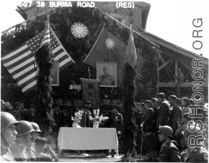 Burma Road dedication ceremony in Kunming, China, on February 4, 1945, during WWII. Review of first convoy (or one of the first convoys) to reach China. General view of the stage and reviewing party, with American and Chinese dignitaries, soldiers, and civilian VIPs. An American band plays, and an honor lines on both sides of the center carpet stand in formation.  Official dignitaries at the ceremony included, on the Chinese side, such figures as General Lung Yun, Governor of Yunnan Province,  Gen. Wang Yu-