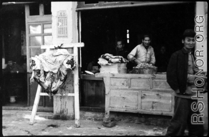 Butcher shop with fresh meat hung to carve in China during WWII.