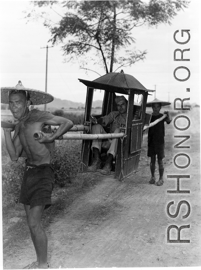 GI rides a sedan chair carried on bamboo poles by two Chinese men. During WWII.