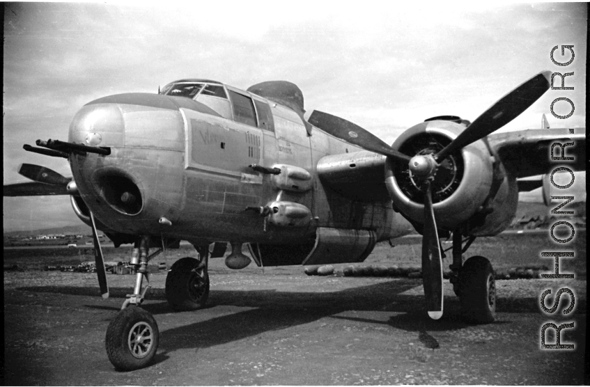 B-25 Mitchell in Yunnan, China, during WWII, with a row of bombs laid out on the ground behind, and bomb  bay doors open.