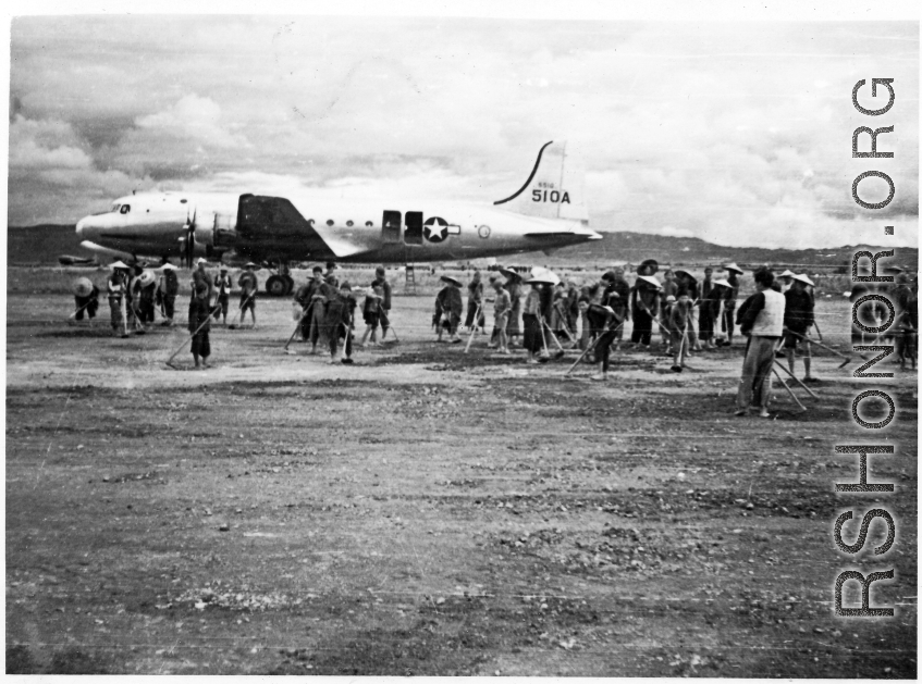Local laborers working on construction of airbase at Luliang, China, with a C-54 transport in background. During WWII.
