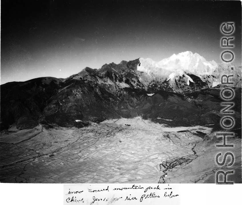 Jade Dragon Snow Mountain (玉龙雪山) with a capping of snow in Yunnan, China, in January as seen from passing American airplane during WWII.  Farm fields and (possibly) rice paddies below.