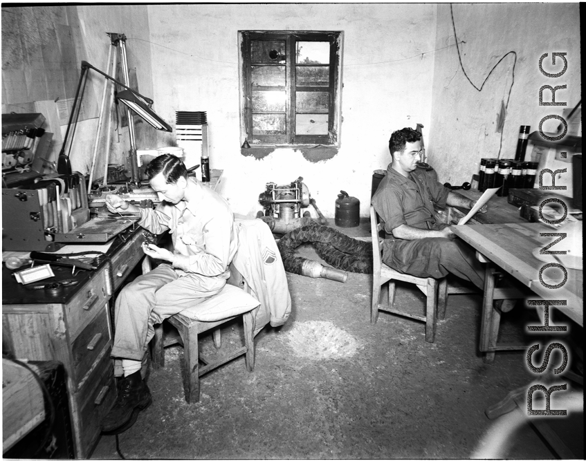 American photographers at work in the workshop in China during WWII. On the left Eugene T. Wozniak repairs a piece of photographic equipment.