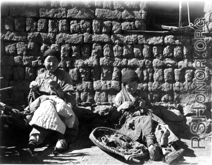 Women in a village in Yunnan mending a cotton blanket and clothing that is little more than rags. During WWII.