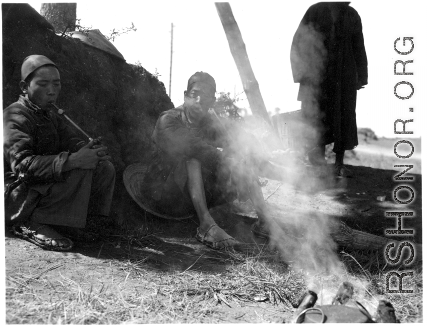 Local people in China: Men smoke and rest in the shade while their food heats over a tiny fire.