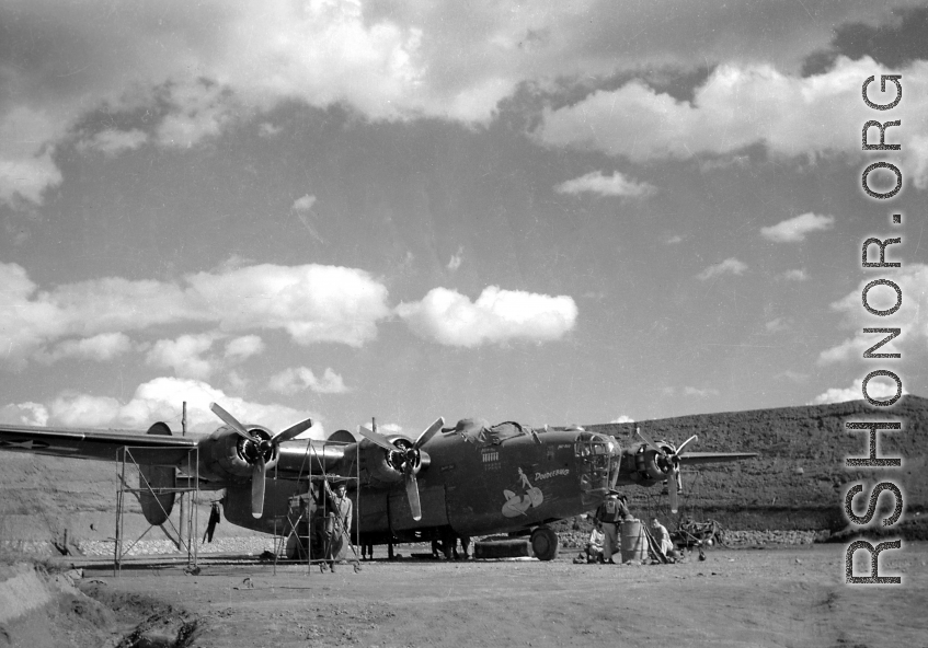 Sichuan (China), B-24 'Doodlebug' being prepared for a mission: "Set in the safety of a reverted hardstand, this B-24 heavy bomber was being readied for a mission. The lady riding a bomb was the trademark of this aircraft named 'Doodlebug' by its crew members. The row of bombs indicate missions carried out. The small Japanese flags represent enemy aircraft shot down. This is an early model plane. Later model B-24's were equipped with a nose gun turret. The turrets provided better target coverage and firepow