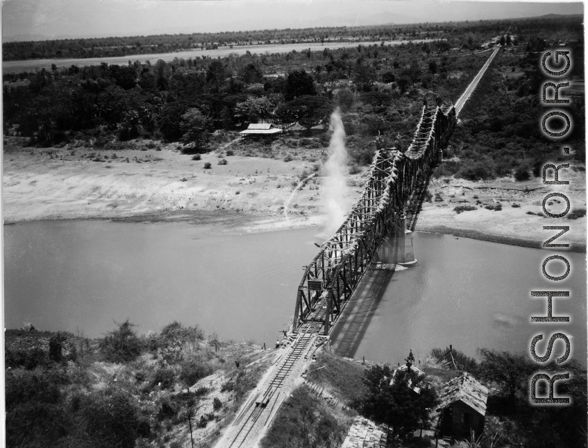 In this image, a bridge somewhere in southwest China, Indochina, or Burma, is bombed by American B-25s, running in very fast at almost tree-top level (notice the perspective of the camera, which is very close to the ground level), with bombs dropping in the river around the bridge. Three to four splash sites can be seen. The bombers come in so fast and unexpectedly that people on the bridge are caught unprepared, as in the blown up image below, where men (either workers or Japanese soldiers) can be seen fra