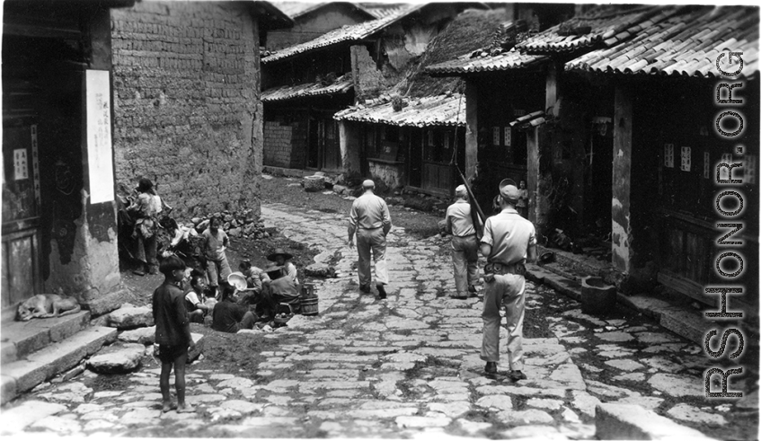 Armed GIs walk on road at Yangkai village, as villagers look up and take note. During WWII.