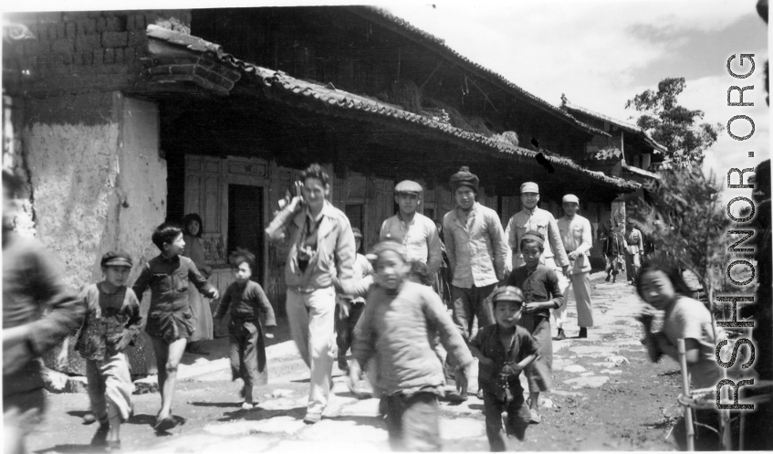 People walk on road at Yangkai village, including  a GI carrying a camera. During WWII.