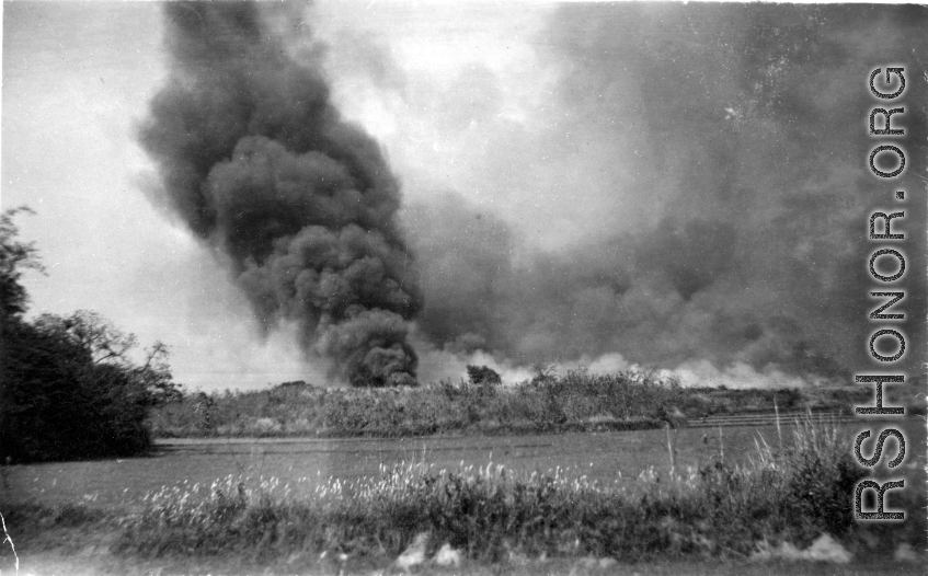 A smoke column arises, and smoke is widely spread about, at an American air base in China during WWII.