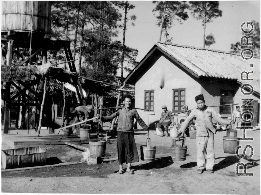 GI explorations of the hostel area at Yangkai air base during WWII: Men haul water in barrels on shoulder poles for use in the hostels.