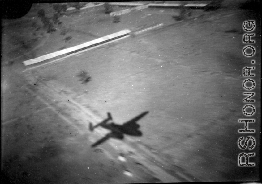 Aerial view of structures and shadow of B-25 in Burma or French Indochina, in the CBI, during WWII.