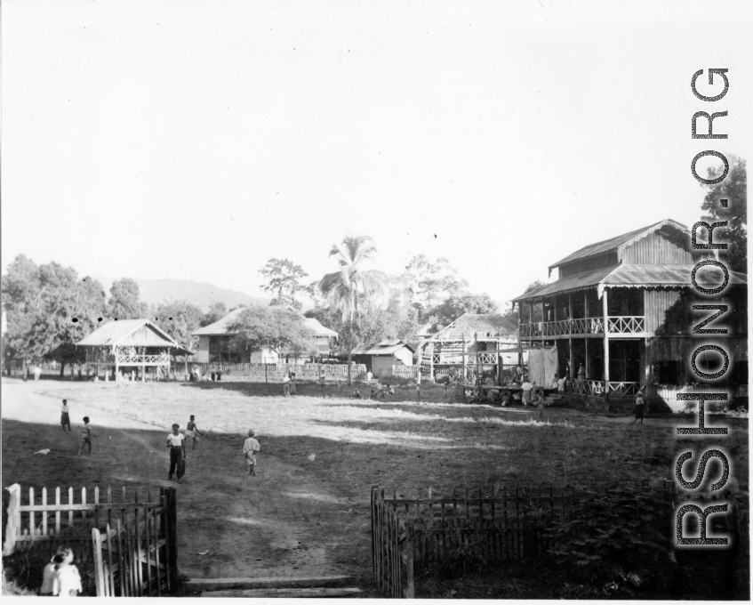 Fence village in Burma. A small crude stage is built in front of the house on the far right.  Near the 797th Engineer Forestry Company.  During WWII.
