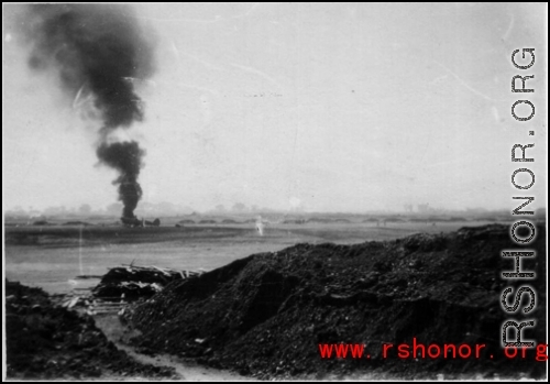 An American airplane burning in the distance after a Japanese air raid. In China, during WWII.