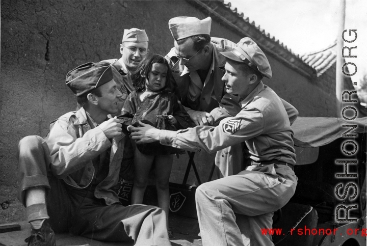 Smiling GIs pose with unhappy small child from poor family in China, during WWII.