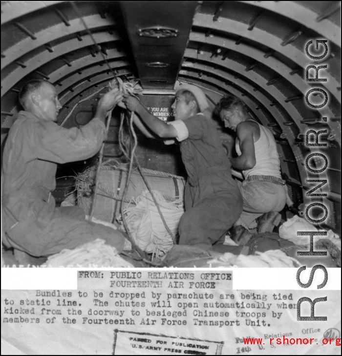Bundles to be dropped by parachute are being tied to static line. The chutes will open automatically when kicked from the doorway to besieged Chinese troops by members of the Fourteenth Air Force Transport Unit.