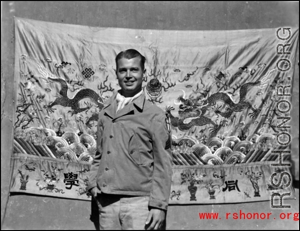 An American serviceman in the CBI, standing in front of an elaborate embroidered silk sheet, during WWII.