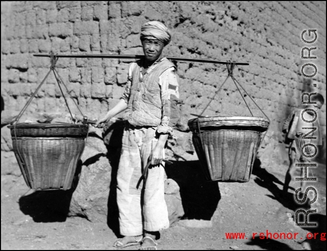 Rural worker with baskets on a shoulder pole. Local people in China, probably in Yunnan province during WWII.