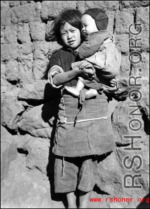 A girl holds a child. Local people in China, probably in Yunnan province.  From the collection of Wozniak, combat photographer for the 491st Bomb Squadron, in the CBI.