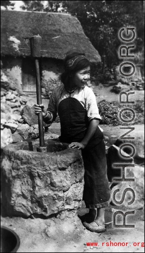 A young woman uses a wooden rod to husk rice in a large stone mortar. Local people in China, probably in Yunnan province.   From the collection of Wozniak, combat photographer for the 491st Bomb Squadron, in the CBI.