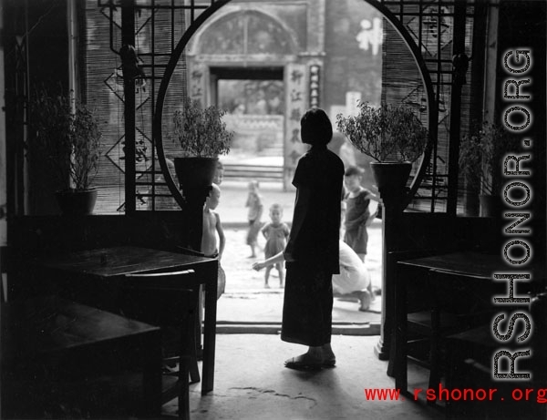 A woman stands in the doorway to a tea house or guild hall or similar meeting place. In Kunming, during WWII.