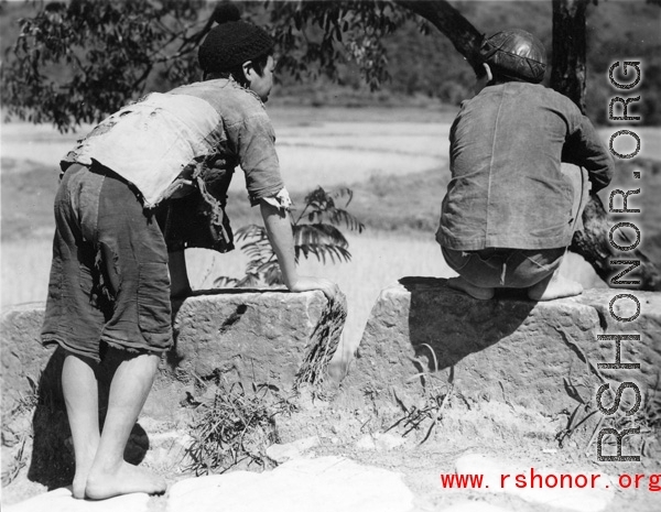 Two boys in China look at something interesting below the road they are on. During WWII.