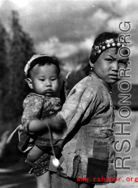 Local people in China: An older sister carries a younger child piggyback as part of her daily responsibilities. During WWII.