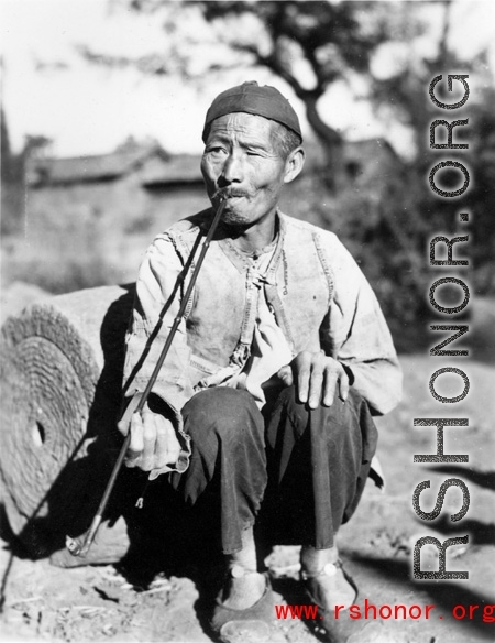 Local man in China during WWII: A man in Yunnan smoking a long pipe. During WWII.